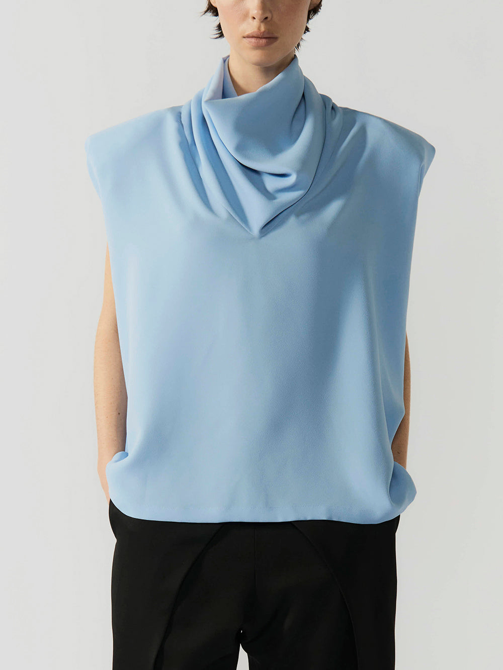 #sky-blue Person wearing a light blue sleeveless top with a cowl neck on a plain background