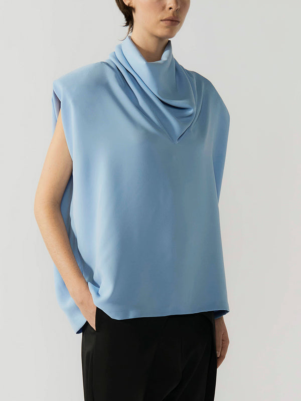 #sky-blue Person wearing a light blue sleeveless top with a brand logo on a plain background