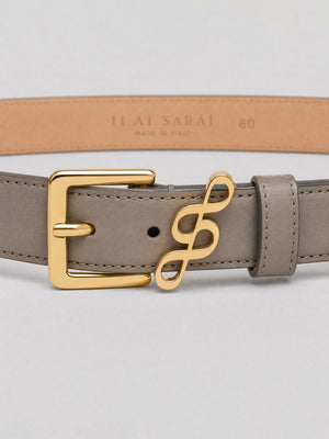 #taupe A taupe leather belt with a polished gold buckle and a decorative gold infinity-style logo clasp, shown against a light gray background with the tan inner band visible.
